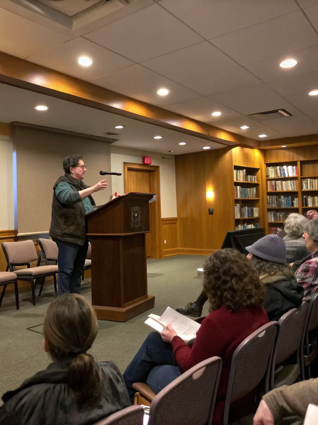 An image showing a literary event with an author giving a reading, surrounded by an attentive audience. The setting should be intimate and engaging, highlighting the importance of literature and intellectual exchange within the community.